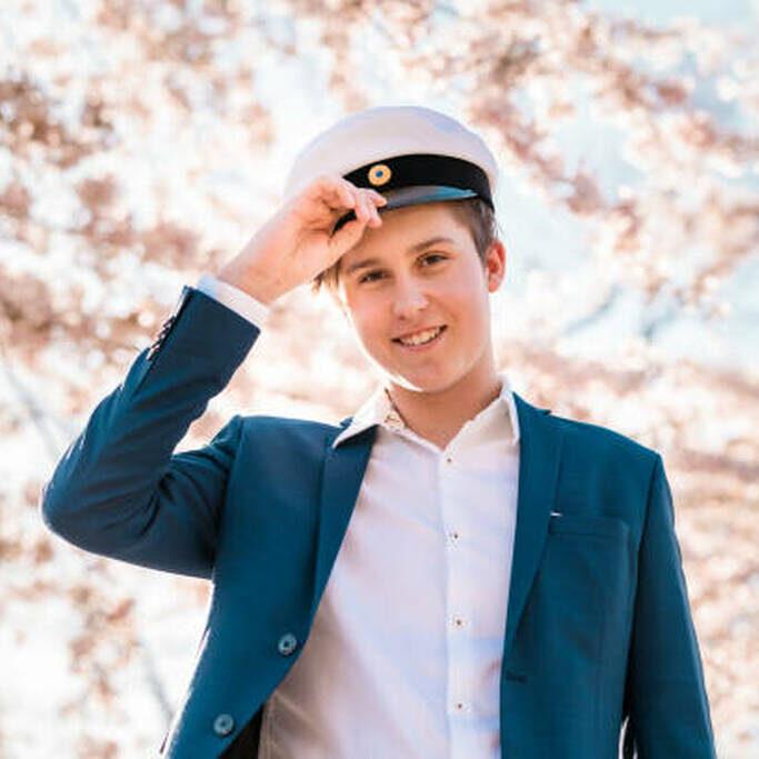 Portrait of a young man wearing his traditional Swedish graduation cap. He is smiling and looking into the camera.